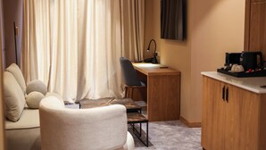 Une pièce de taille modeste comprenant un canapé, un bureau, une chaise, un téléviseur et une machine à café.