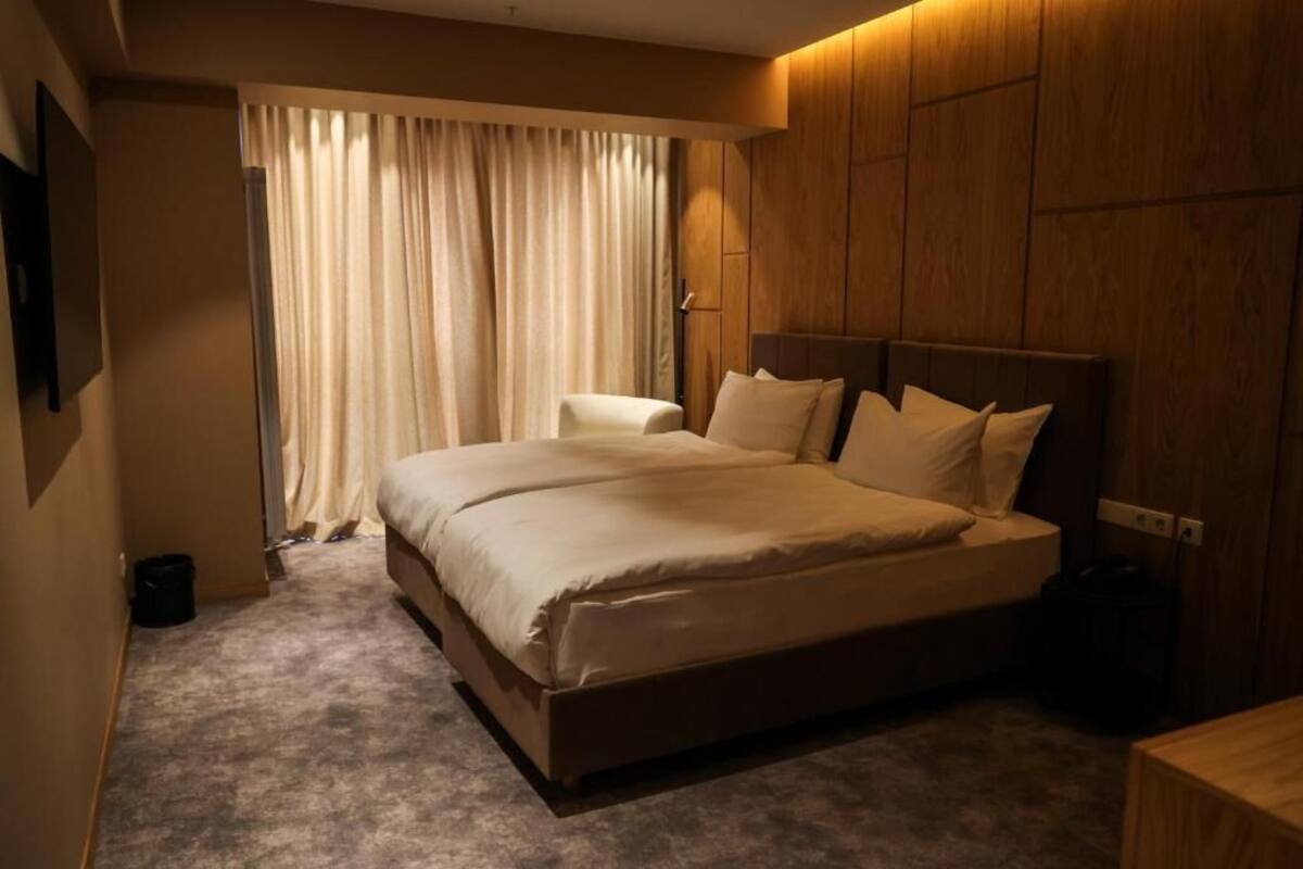 Ein Hotelzimmer mit einem großen Bett, einem Holzkopfteil, einem Nachttisch und einem Fenster mit Vorhängen.