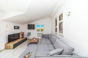 Ein modernes Wohnzimmer mit einem grauen Sofa, einem Flachbildfernseher, einem Holztisch und einem Bücherregal.