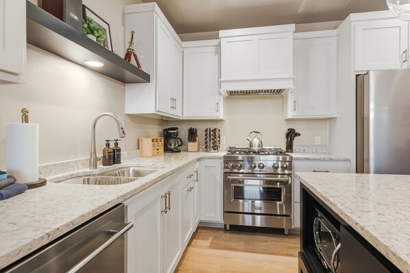 A modern kitchen with white cabinets, stainless steel appliances, and a marble countertop.