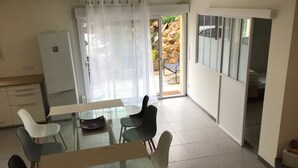 Una zona de menjador amb taula i cadires de vidre, un frigorífic i una porta corredissa de vidre que dona a una zona exterior amb cotxe i un mur de roca.