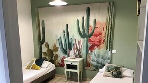 Un dormitori amb dos llits, una tauleta de nit i un mural de paredad amb temàtica de cactus.