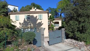 Una casa de dos pisos amb un carrer d'accés tancat per una reixa, envoltada de vegetació i arbres.