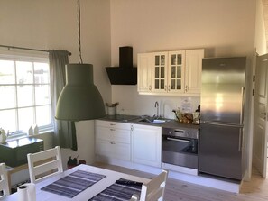 A compact kitchen with white cabinets, a stainless steel refrigerator, a built-in oven, and a hanging pendant light. - 5 Star Holiday Home in Ansager (Ansager)