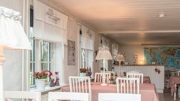 A cozy dining area with white chairs and pink tablecloths, featuring a world map on the wall and a small table with flowers and a lamp. - 5 Star Holiday Home in Ansager (Ansager)