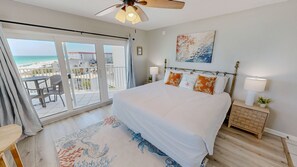 A bedroom with a large bed, a balcony with a view of the beach, a ceiling fan, and a nightstand with a lamp. - Seacrest 601a Condo (Fort Walton Beach)
