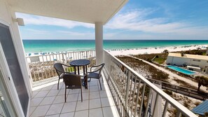 A balcony with a view of the beach, a pool, and a building with a flat roof. - Seacrest 601a Condo (Fort Walton Beach)