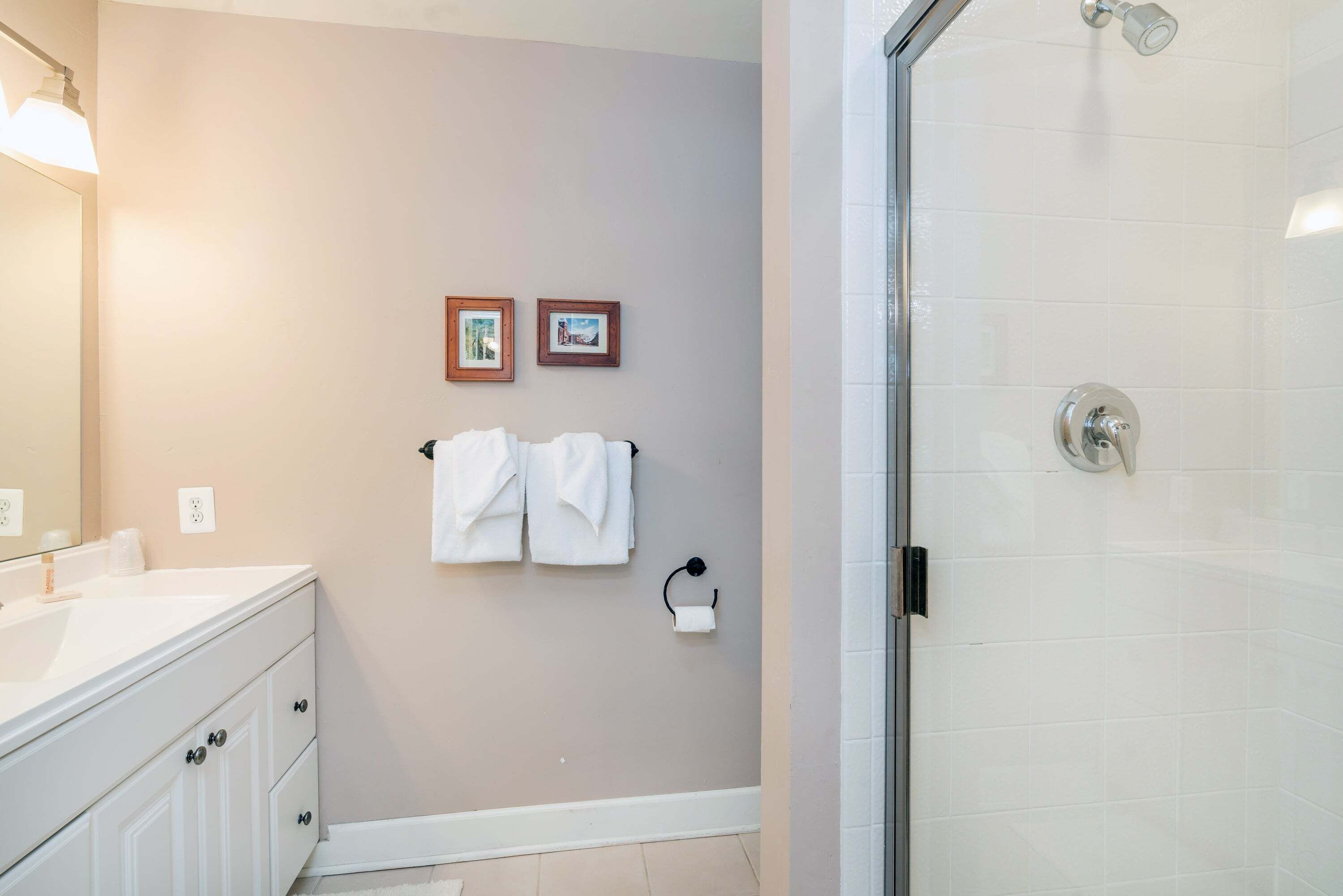 A bathroom with a white vanity, a glass shower enclosure, and two framed pictures on the wall.
