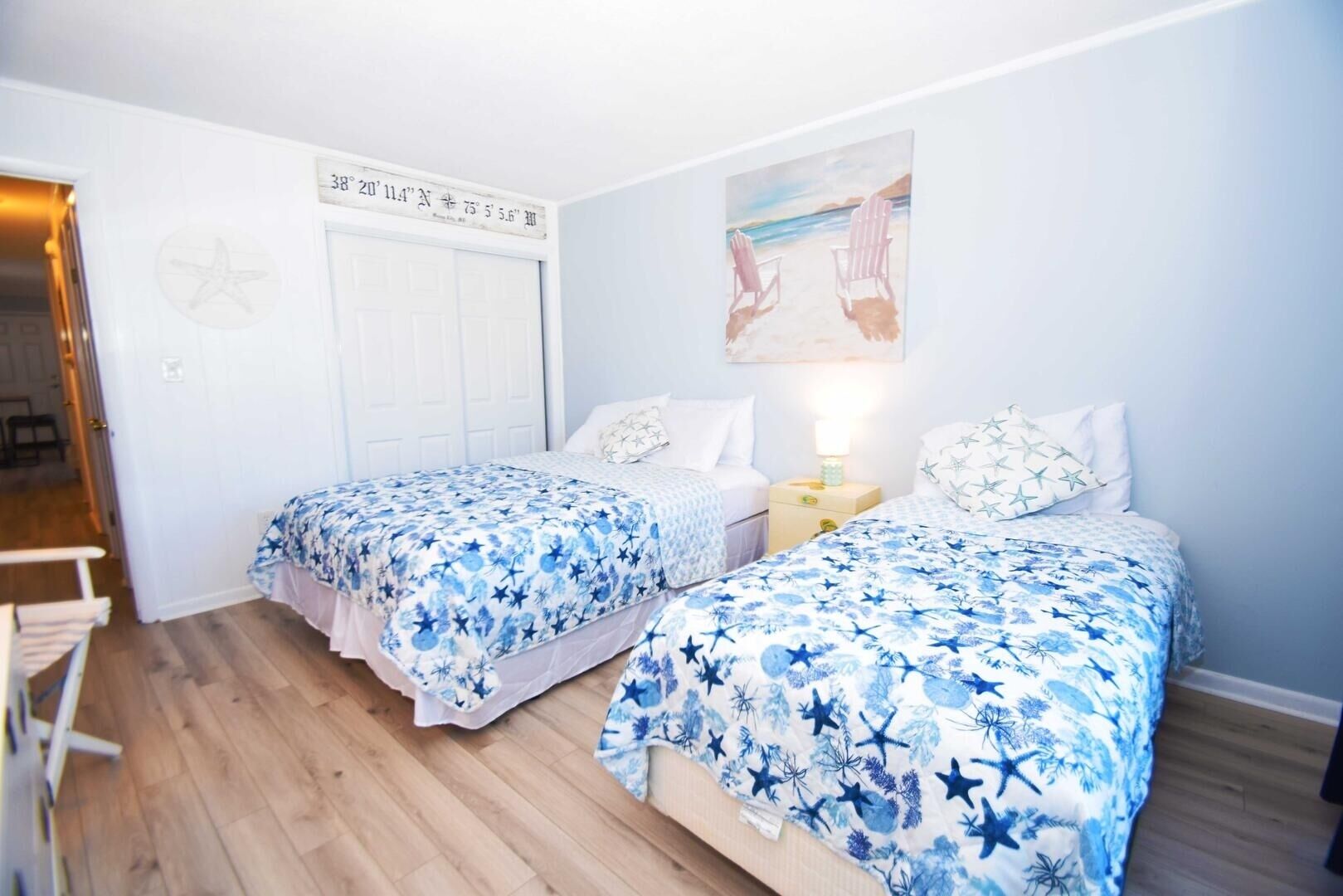 A bedroom with two beds, a star map on the wall, and a painting of a beach scene.