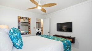 Ein Hotelzimmer mit Bett, Fernseher, Deckenventilator, Spiegel und Tür zu einem Badezimmer.