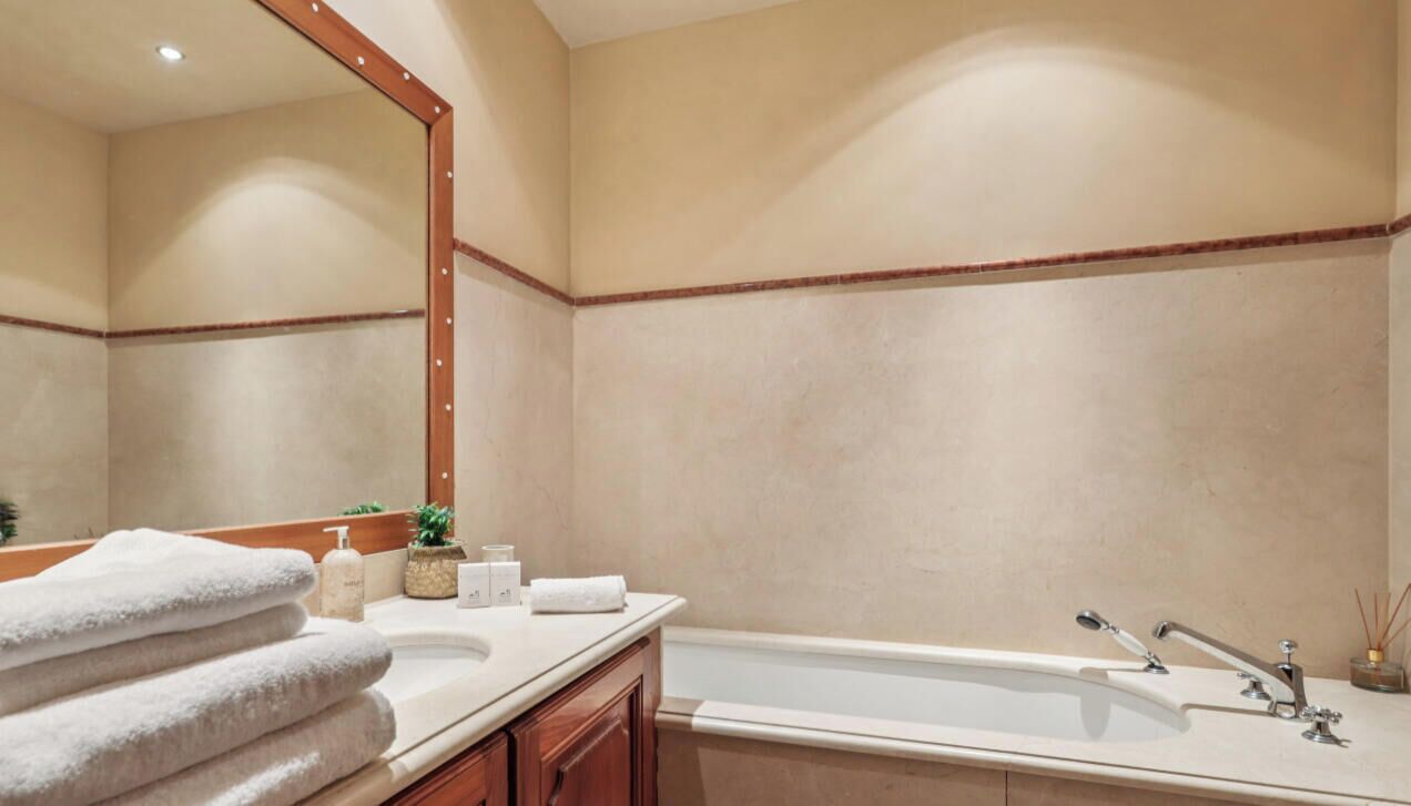 A bathroom with a bathtub, a large mirror, and a vanity with toiletries.