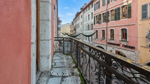 Ein schmaler Gang mit schmiedeeisernem Balkongeländer, gesäumt von Gebäuden mit traditioneller europäischer Architektur und Fensterläden.