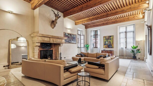 Ein geräumiges Wohnzimmer mit Kamin, Ledersofas und einer hohen Holzbalkendecke.