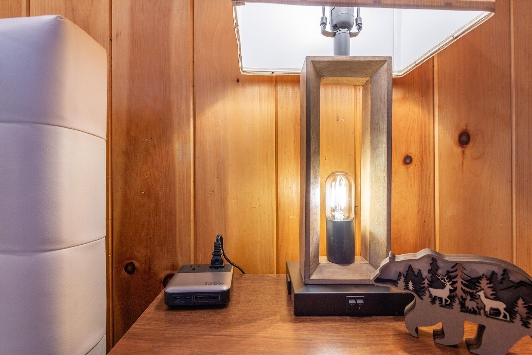 Une pièce aux murs lambrés, comprenant un bureau, une lampe, une multiprise et un objet décoratif en bois.