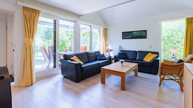 A spacious living room with a large sliding glass door, two black sofas, a wooden coffee table, and a wicker chair. - Westduin Apartment Near the Beach (Vlissingen)