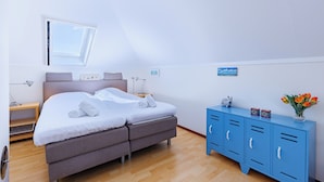A bedroom with a bed, a blue wardrobe, a nightstand, and a window. - Westduin Apartment Near the Beach (Vlissingen)