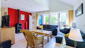 A modern living room with a fireplace, a sofa, a dining table, and a television. - Westduin Apartment Near the Beach (Vlissingen)