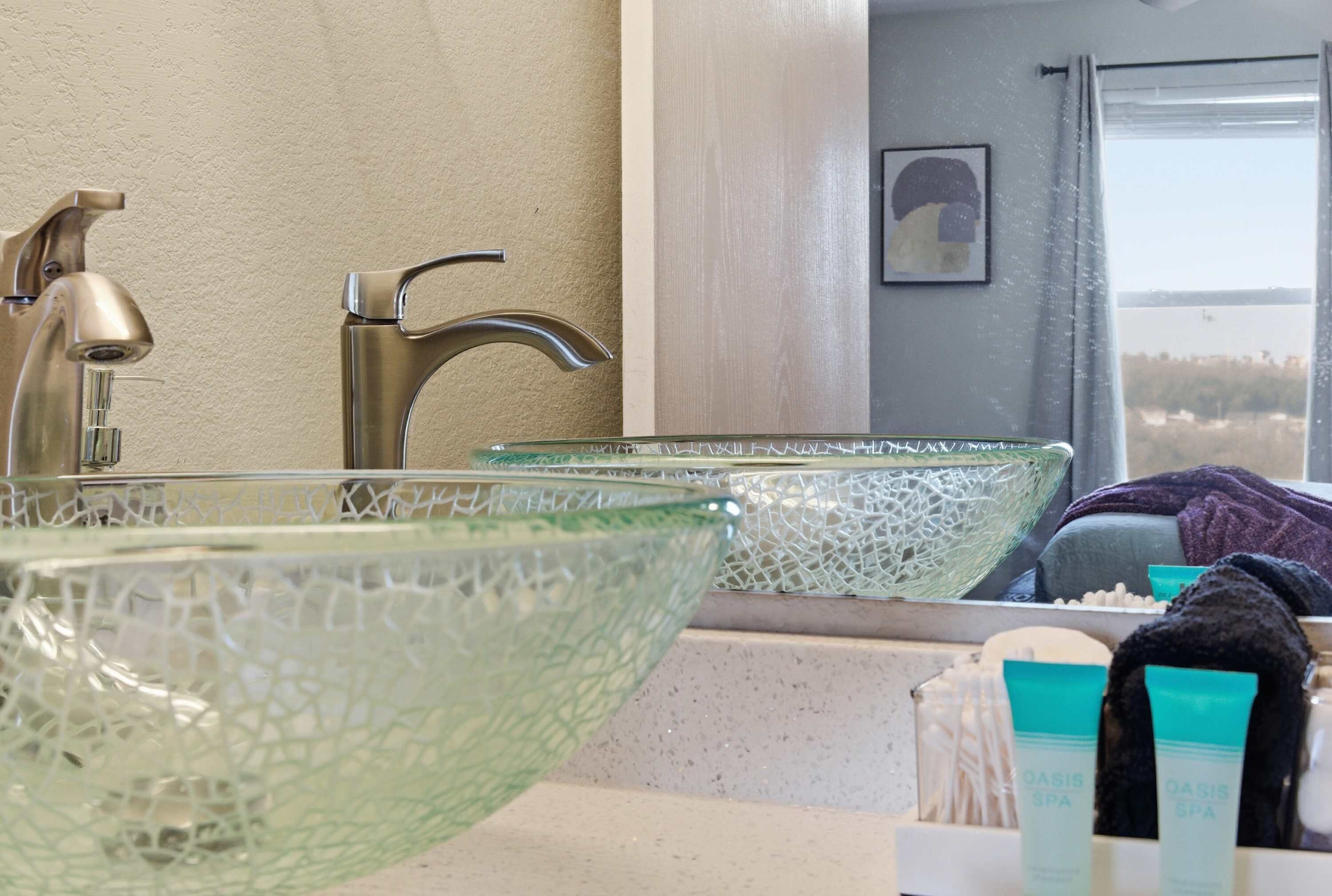 A bathroom with a glass bowl sink, a mirror, and toiletries.