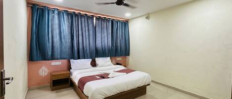 Un dormitorio con cama, mesita de noche, ventilador de techo y ventana con cortinas.