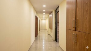A corridor with wooden cabinets and doors, a tiled floor, and recessed ceiling lighting. - Hotel Sun Stay Ahmedabad (Ahmedabad)