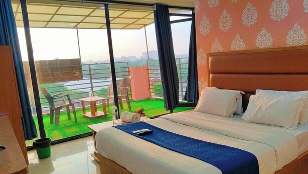 A hotel room with a large bed, a balcony with chairs, and a view of the city. - Hotel Sun Stay Ahmedabad (Ahmedabad)