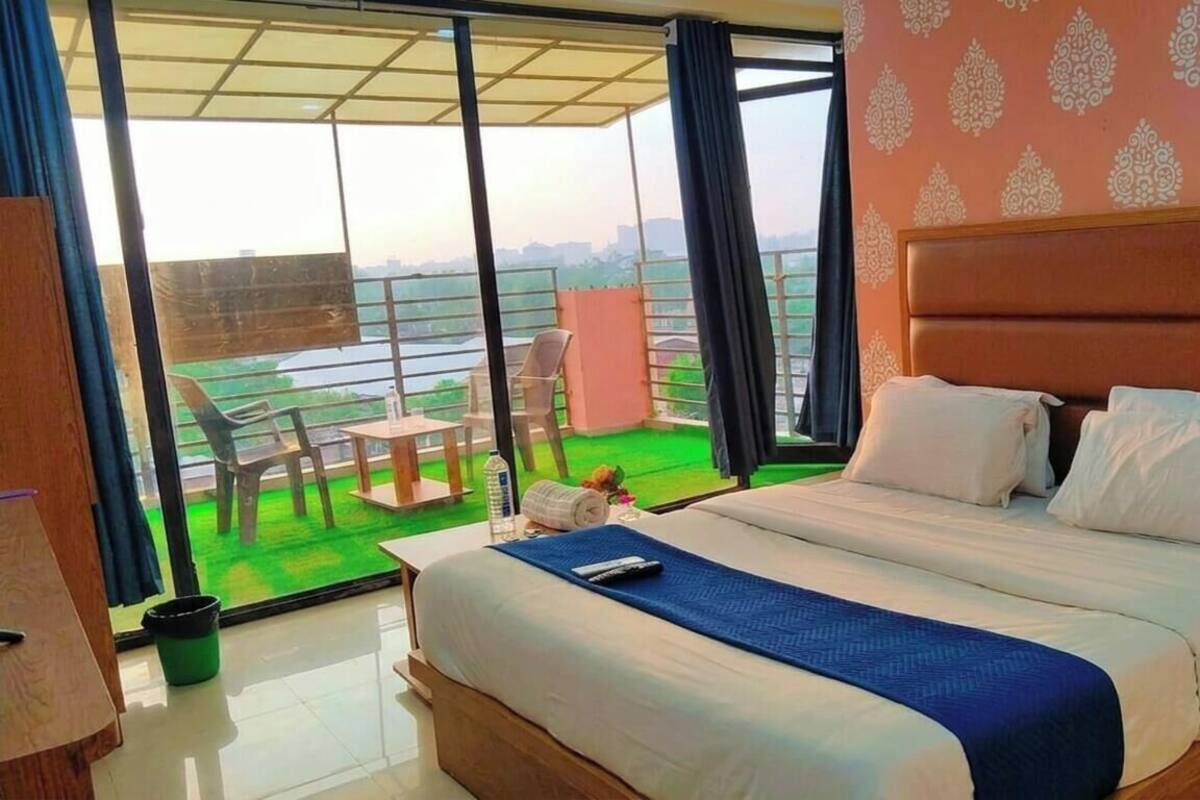 Une chambre d’hôtel avec un grand lit, un balcon avec des chaises et une vue sur la ville.