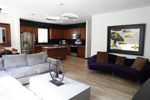 A modern kitchen with stainless steel appliances, a wooden island, and a dining area with a white table and purple sofa. - Designer Luxury Near Downtown Concord/Charlotte, NASCAR, and Renaissance Fair (Concord)