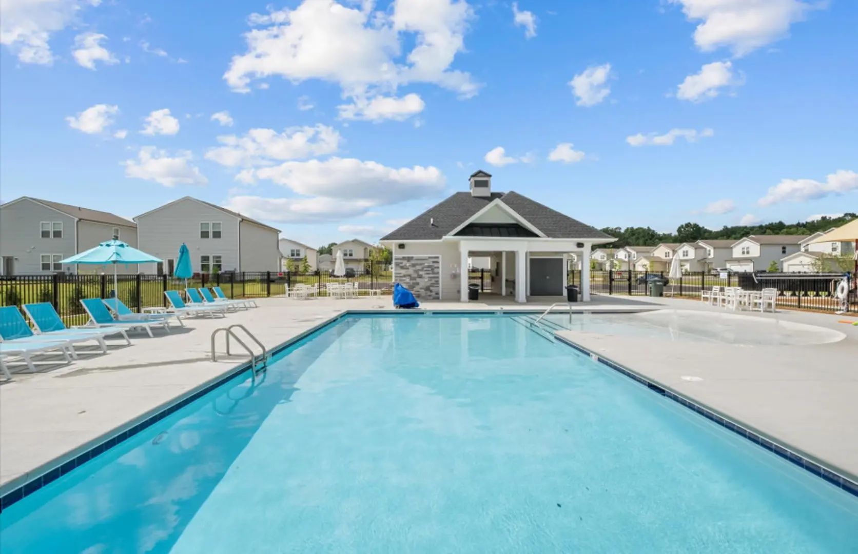 A swimming pool with lounge chairs and a covered area, surrounded by residential buildings.