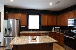 A modern kitchen with wooden cabinets, stainless steel appliances, a granite countertop, and a window providing natural light. - Designer Luxury Near Downtown Concord/Charlotte, NASCAR, and Renaissance Fair (Concord)