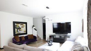 Un salon moderne avec un canapé gris, un canapé violet, un téléviseur à écran plat et une table basse.