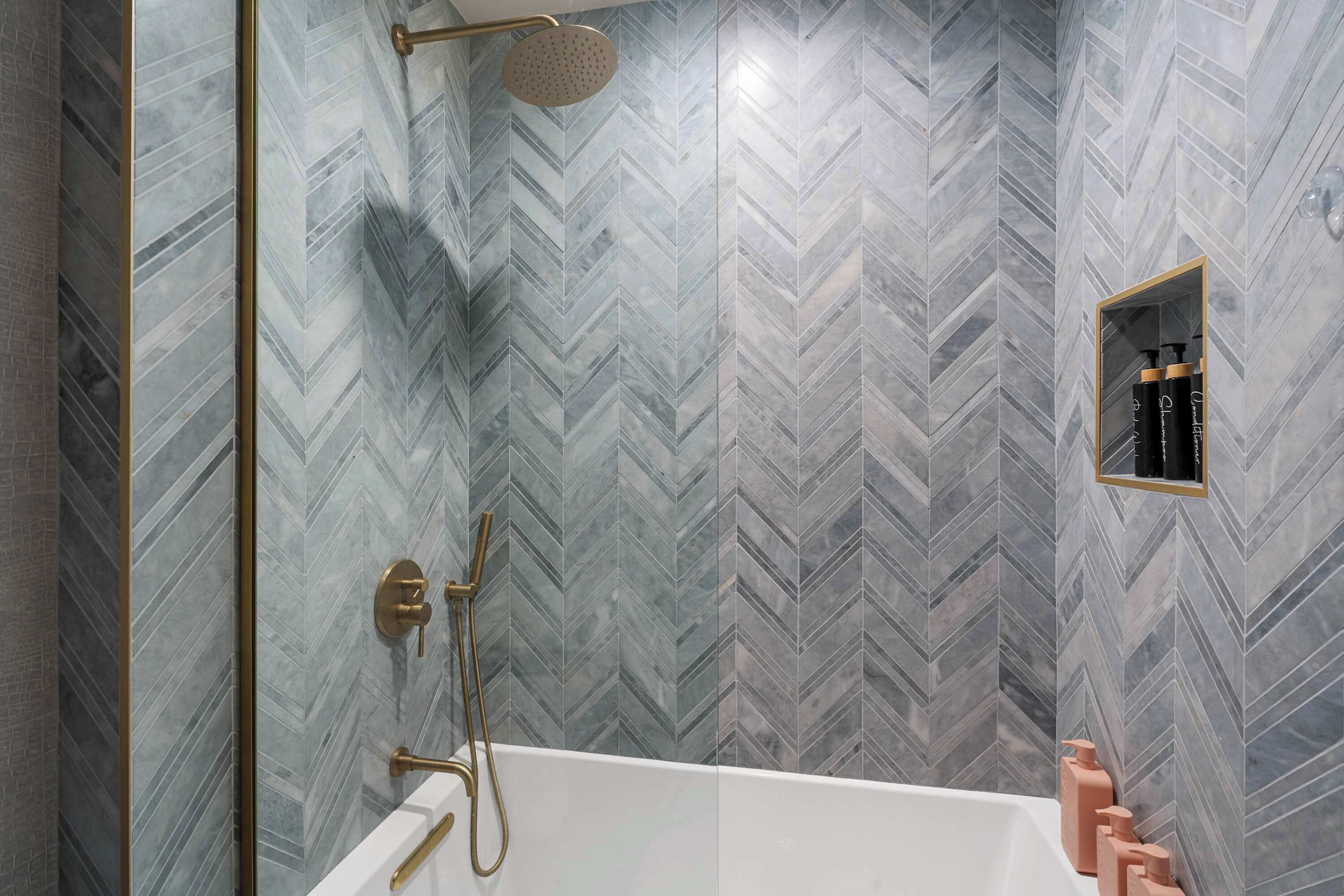 A modern bathroom with a herringbone tile pattern, a freestanding bathtub, and a gold showerhead.