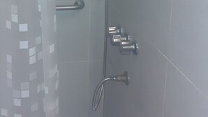 Une douche avec une porte en verre, un pommeau de douche à main et un robinet fixé au mur.