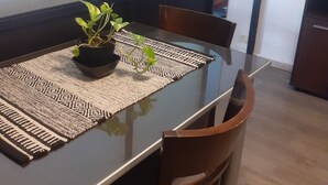 Une table à manger avec un plateau en verre noir, un set de table en fibres tressées et une plante en pot.