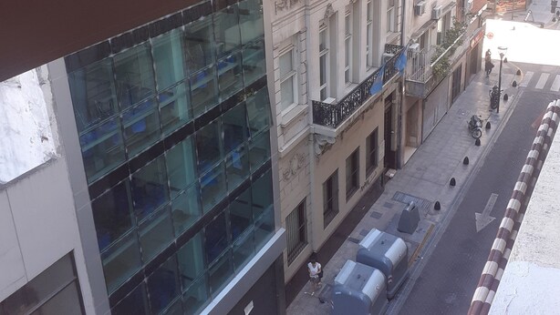 Un immeuble de grande hauteur doté d’une façade moderne en verre, une rue étroite en contrebas et une promenade piétonne.