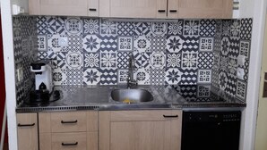 A kitchen with light wood cabinets, a black countertop, a patterned backsplash, and a black dishwasher. - 4/6-person apartment, 5 floors with elevator (Dévoluy)