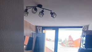 A compact room with a dining table, chairs, a small sofa, and a window with a view of buildings. - 4/6-person apartment, 5 floors with elevator (Dévoluy)