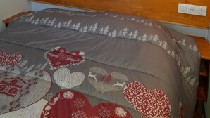 A bedroom with a wooden headboard, a bed with a patterned bedspread, a wall-mounted painting of a snowy mountain landscape, and two wall-mounted reading lights. - 4/6-person apartment, 5 floors with elevator (Dévoluy)