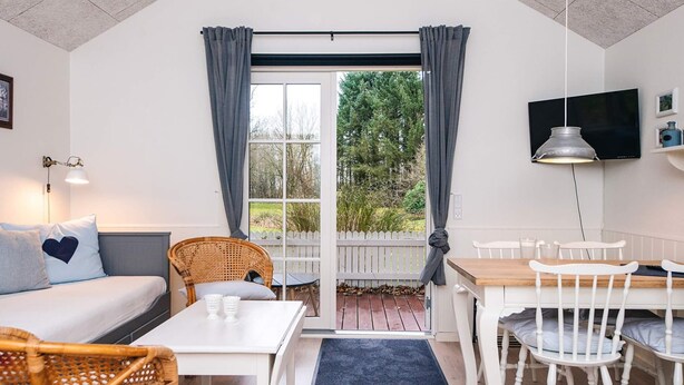 A cozy room with a bed, a dining table, and chairs. There is a TV mounted on the wall and a window with curtains. - 5 Star Holiday Home in Ansager (Ansager)