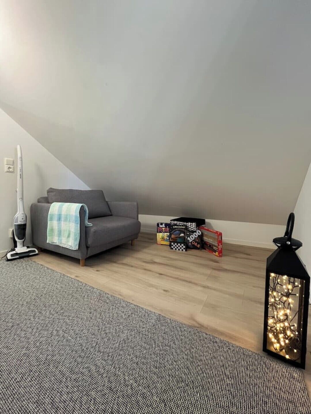 Un apartamento tipo loft con un sofá gris, un aspirador, una lámpara y algunas cajas en el suelo.