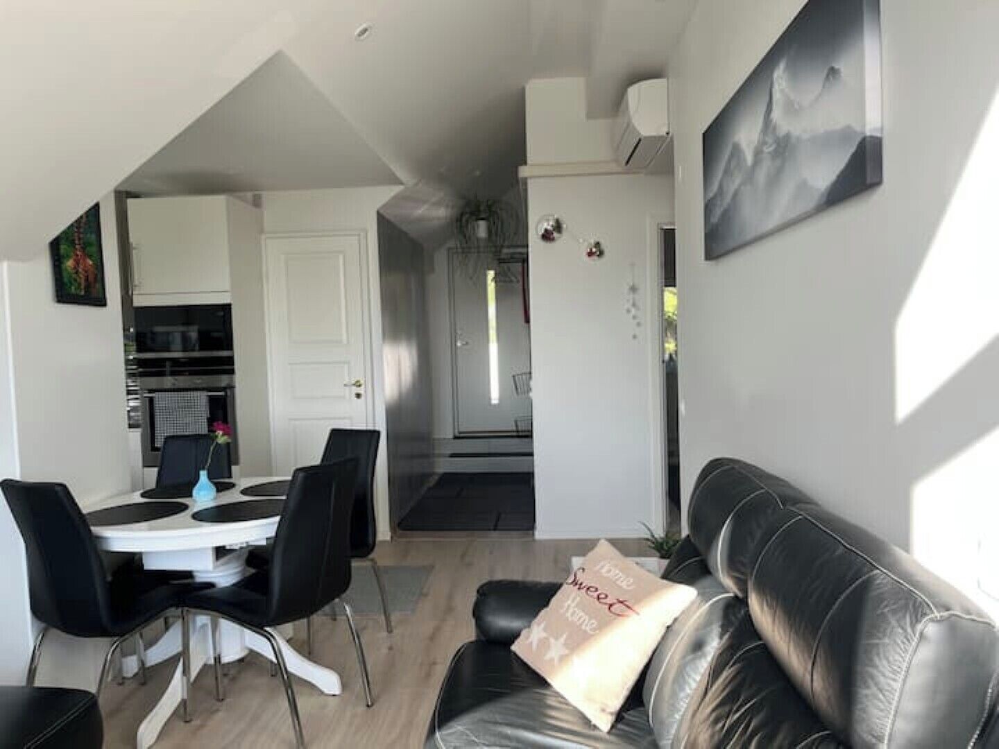 Een moderne woonkamer met een zwarte leren bank, een eethoek met een witte tafel en zwarte stoelen, en een keuken op de achtergrond.