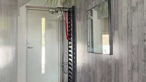 En modern hall med en väggpanel av trä, en vit dörr, ett svart metallstaket, en krukväxt och en spegel.