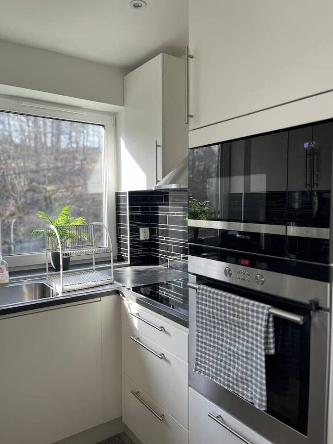 Una cocina moderna con ventana, electrodomésticos de acero inoxidable y vista a árboles.