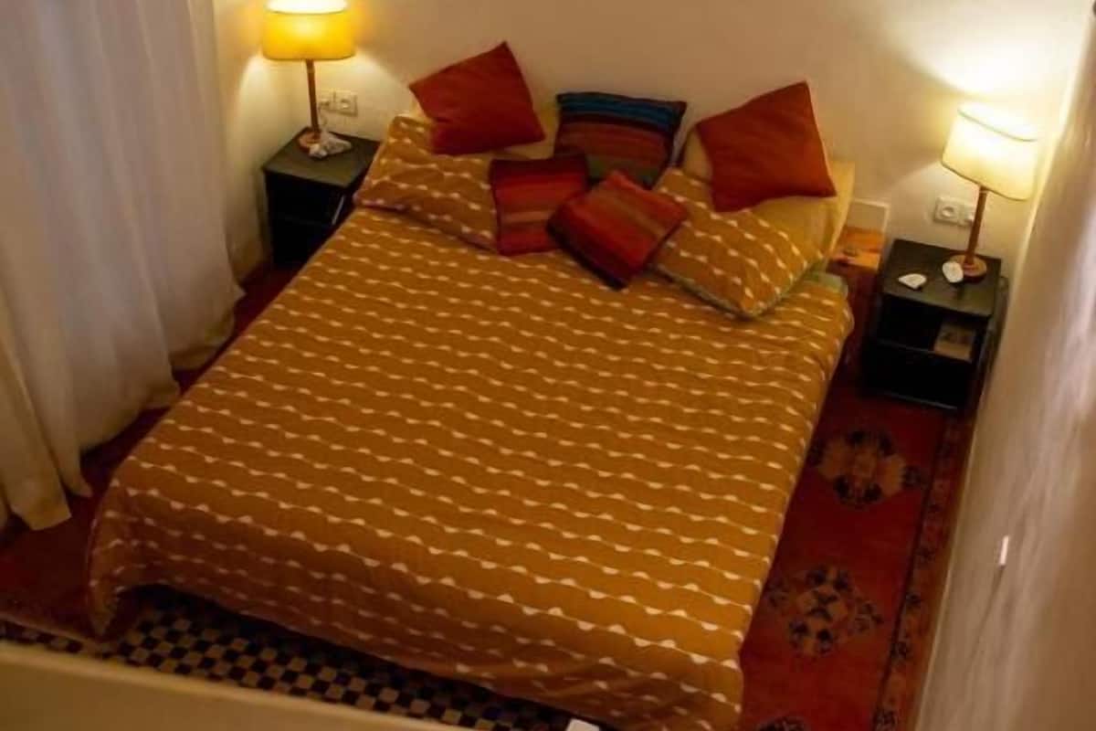 A bedroom with a bed, two bedside tables, a nightstand, a patterned rug, and a staircase.