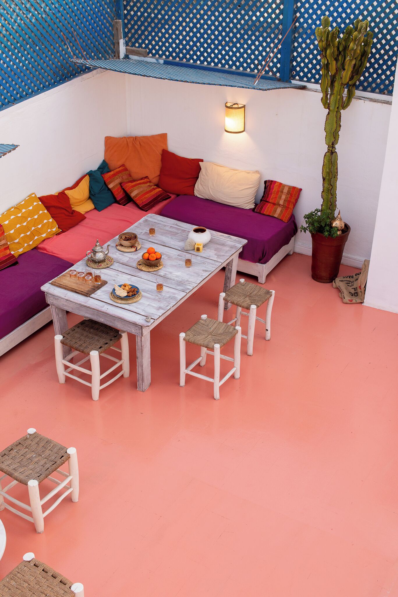 Un espacio al aire libre acogedor con una mesa de madera, cojines coloridos y un cactus en maceta.