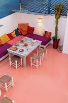 Un espacio al aire libre acogedor con una mesa de madera, cojines coloridos y un cactus en maceta.