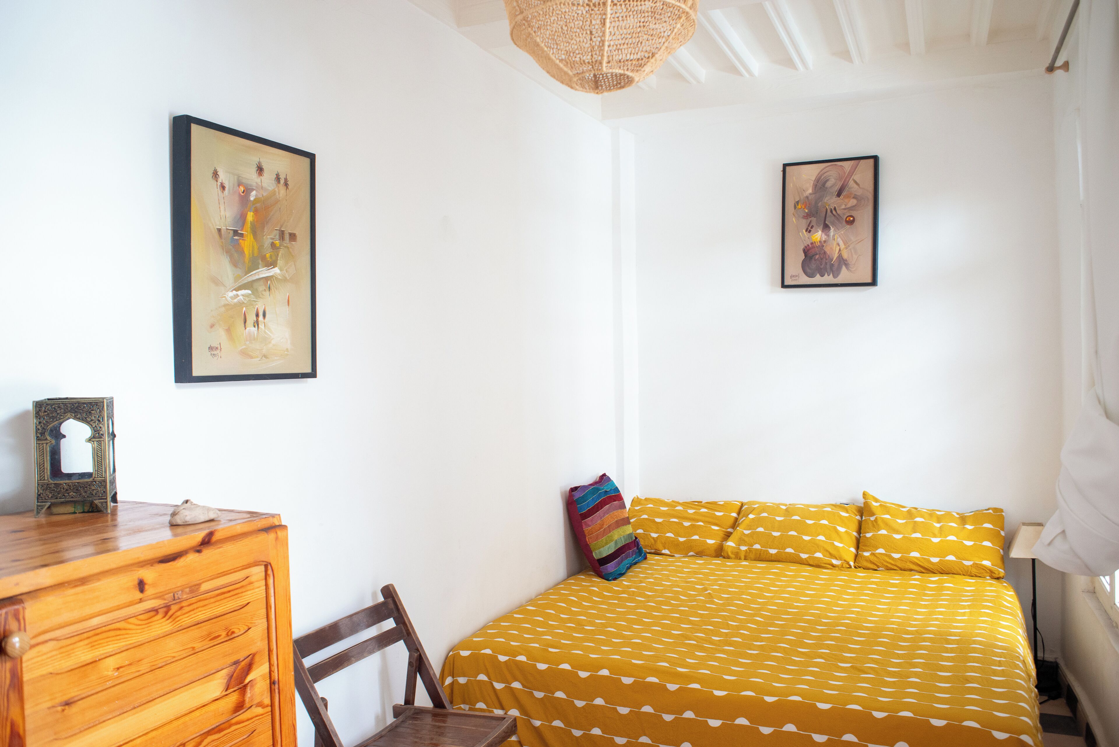 Ein Schlafzimmer mit einem Bett, einer Holzkommode und zwei gerahmten Kunstwerken an der Wand.