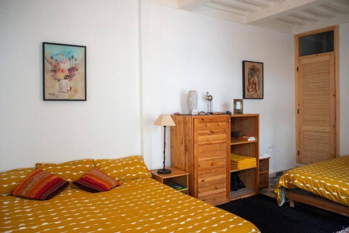 A bedroom with two beds, a wooden wardrobe, and artwork on the walls.