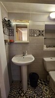 Un baño con un lavamanos blanco, un espejo y un inodoro. El piso presenta un diseño de baldosas geométricas.