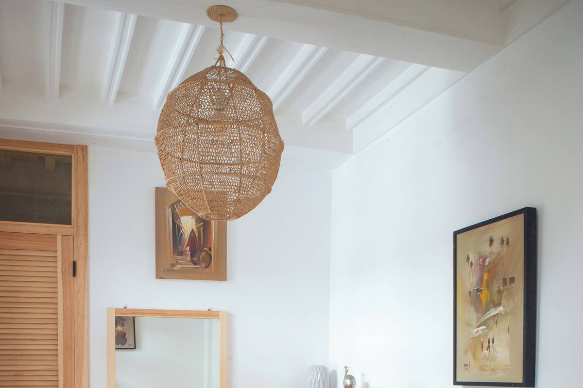 A room with a checkered floor, a wooden wardrobe, a mirror, a hanging light fixture, and a chair.