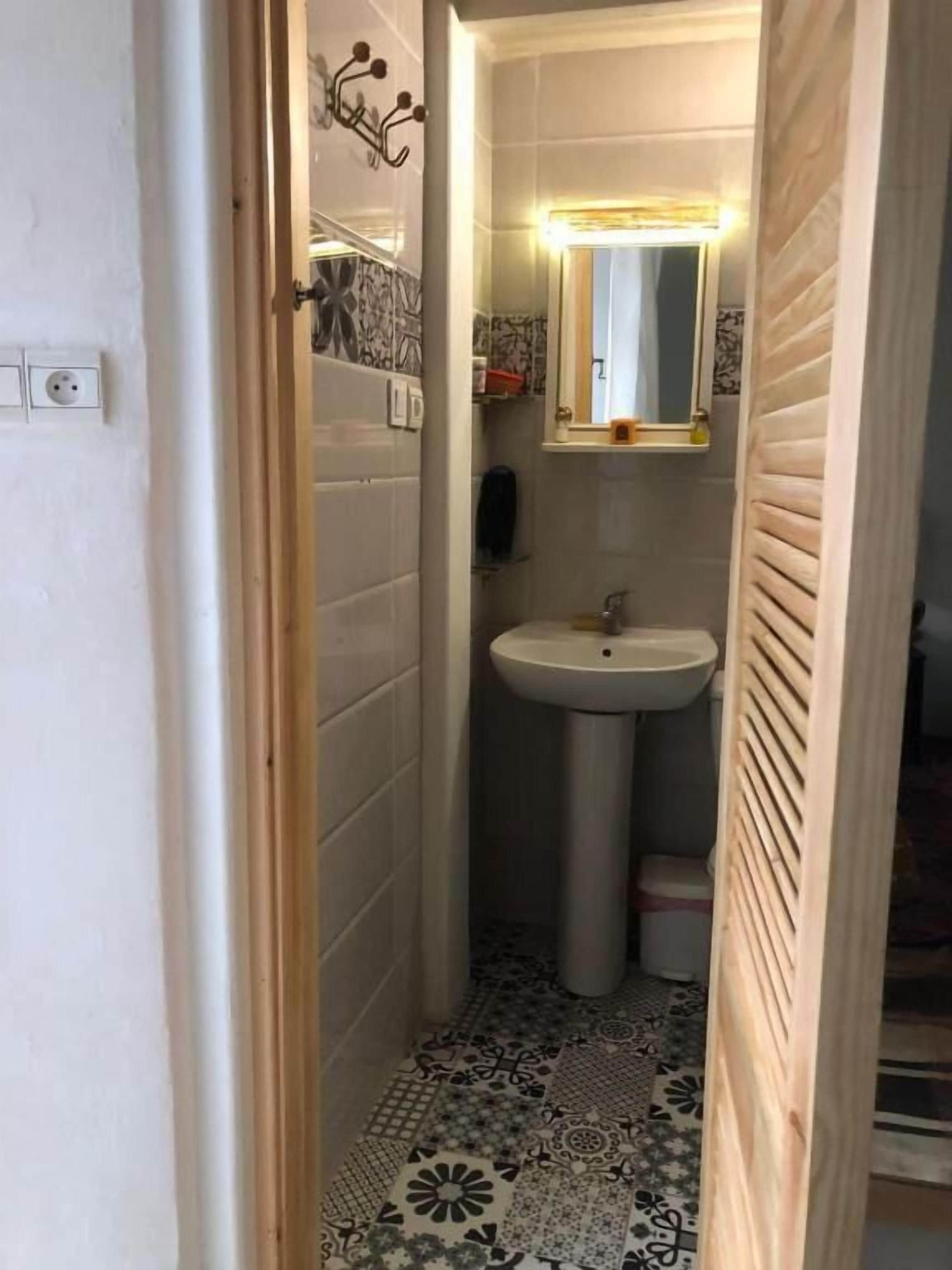 Une petite salle de bain avec un lavabo sur colonne, un miroir et des carreaux de sol à motifs.